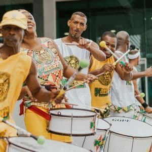 Un gruppo di musicisti in abiti coordinati gialli e bianchi suona grandi tamburi bianchi durante uno spettacolo all'aperto.