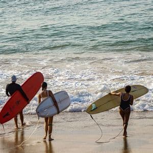 Un viaggio di gruppo WeRoad con tre surfisti che, tavole in mano, si avviano verso le dolci onde dell'oceano da una spiaggia di sabbia.