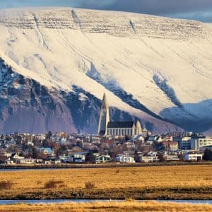 Una città con una chiesa imponente si trova ai piedi di una massiccia montagna innevata sotto un sole splendente.