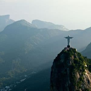 La statua del Cristo Redentore si erge su una cima di montagna, dominando un vasto paesaggio di montagne verdi e sfumate.