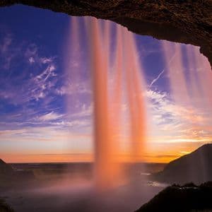 Una vista a lunga esposizione da dietro una cascata, illuminata da un tramonto colorato su una valle.