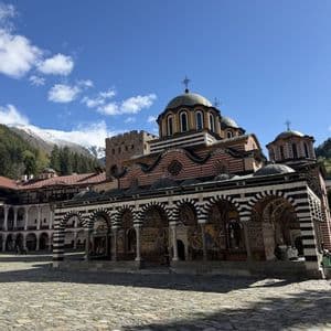 Un grand monastère orné avec des arches et des dômes rayés dans une cour pavée, avec une montagne enneigée en arrière-plan.