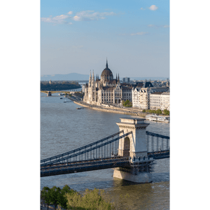Un ponte a catena storico attraversa un ampio fiume, con un palazzo del parlamento ornato e a cupola sulla riva opposta sotto un cielo blu.