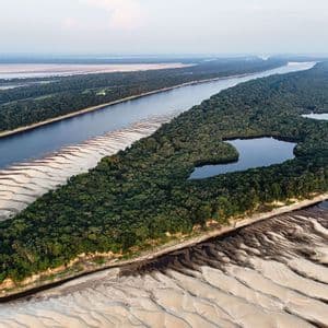 Veduta aerea di un grande fiume con banchi di sabbia bianca affioranti che circonda un'isola di fitta foresta verde contenente una piccola laguna.