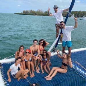 Amici in viaggio di gruppo WeRoad, sorridenti e in posa sulla rete di un catamarano in mare.