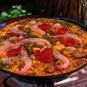 Un primo piano di una paella tradizionale in una grande padella nera, ricca di gamberi, peperoni rossi e fagiolini.