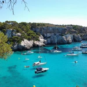Una vista dall'alto di barche che galleggiano in una cala con acqua turchese, circondata da scogliere rocciose coperte di alberi verdi.