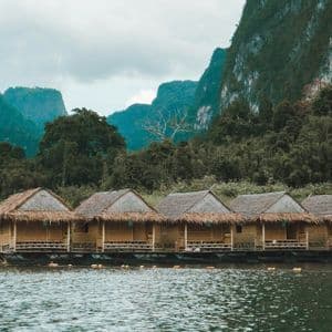 Una fila di bungalow galleggianti con tetti in paglia si trova su un lago ai piedi di montagne ricoperte dalla giungla.