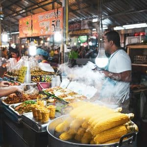 Una grande pentola di pannocchie fumanti si trova su una bancarella in un vivace mercato coperto.