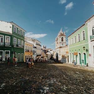 Una larga strada acciottolata, fiancheggiata da colorati edifici coloniali, con persone che passeggiano in una giornata di sole.
