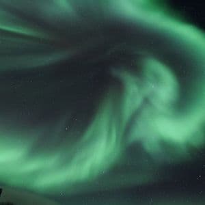 L'aurora boreale verde si libra in un cielo notturno buio e stellato, sopra una sagoma rocciosa all'angolo.