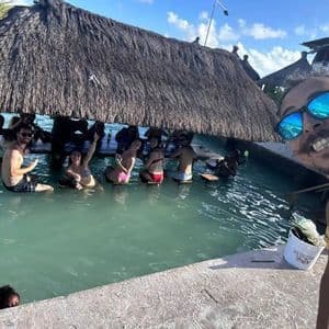 Un uomo scatta un selfie mentre un gruppo WeRoad si gode un momento di relax in un bar a bordo piscina con tetto di paglia.