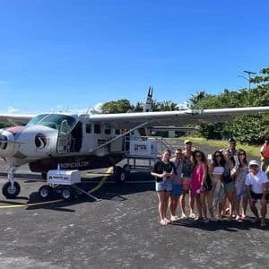 A WeRoad group trip posing for a photo on an airfield tarmac in front of a small propeller plane.