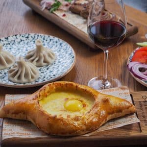 Un pasto tradizionale georgiano con Khachapuri Adjaruli, Khinkali e un bicchiere di vino rosso su un tavolo di legno.