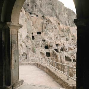 Una vista da un arco in pietra di numerose grotte artificiali scavate in un'imponente parete rocciosa.
