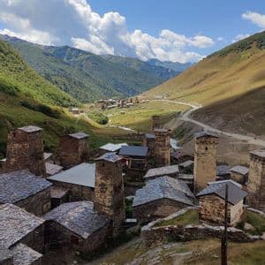 Un borgo di case in pietra e torri adagiato in una verde valle montana sotto un cielo parzialmente nuvoloso.