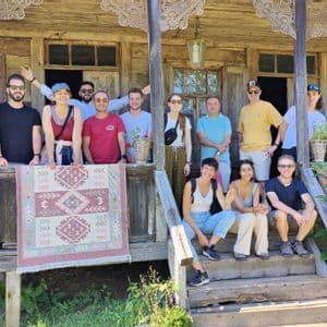 Un gruppo WeRoad in posa per una foto sul portico e sui gradini di una casa rustica in legno, con in mano un tappeto a motivi.