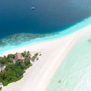 Veduta aerea di un lembo di sabbia bianca con palme ed edifici, che divide l'oceano blu intenso dalle acque turchesi poco profonde.