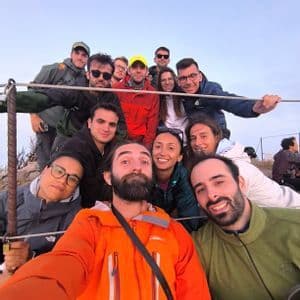 Un viaggio di gruppo WeRoad con persone sorridenti, in giacche da esterno, che posano per un selfie di gruppo su una collina.