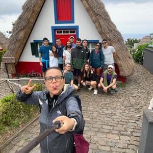 Un gruppo WeRoad posa per un selfie davanti a tradizionali case con tetti di paglia su un sentiero di ciottoli.
