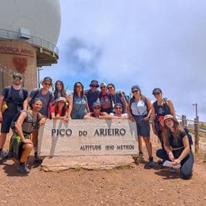 Un gruppo WeRoad in viaggio si scatta una foto nei pressi del segnale di vetta del Pico do Arieiro, su una montagna.