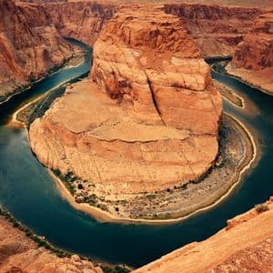 Veduta aerea di un fiume che si incurva a ferro di cavallo attorno a un grande faraglione di roccia rossa all'interno di un canyon.