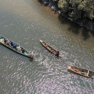 Una vista aerea di un viaggio di gruppo WeRoad su un'imbarcazione tradizionale su un fiume scintillante, con due canoe locali più piccole nelle vicinanze.