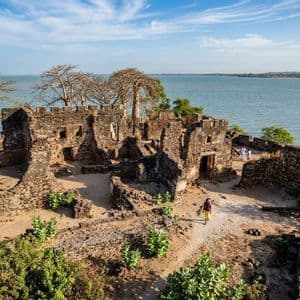 Vista aerea delle rovine in pietra di un'antica fortezza su una collina affacciata sull'acqua, con una persona che cammina su un sentiero.