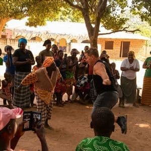 Un membro del gruppo WeRoad balla con una donna locale mentre altri osservano, applaudono e suonano i tamburi in un villaggio.