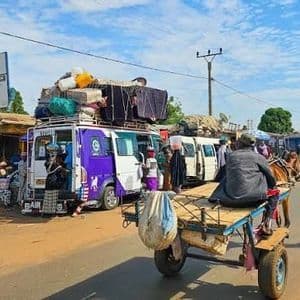 Una strada trafficata con un carro trainato da cavalli, persone che camminano e una fila di minibus carichi di bagagli sui tetti.