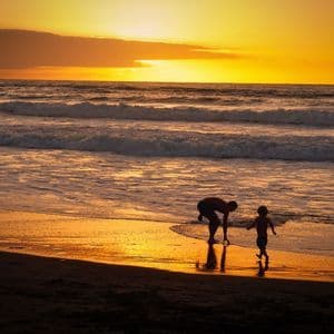 Un adulto e un bambino in silhouette giocano su una spiaggia bagnata dall'oceano durante un tramonto dorato.