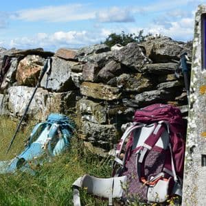 Zaini e bastoncini da trekking poggiano contro un muro di pietra accanto a un segnavia del Cammino di Santiago.