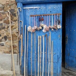Bastoni da passeggio in legno e collane di conchiglie sono esposti in vendita davanti a una luminosa porta di legno blu.