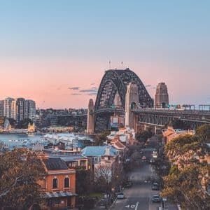Sydney Harbour Bridge at sunset The Sydney Harbour Bridge and the city rooftops under a pink and orange sunset sky.