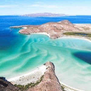 Una vista aerea di una costa rocciosa con spiagge di sabbia bianca, circondata da acque turchesi e dal blu intenso del mare.