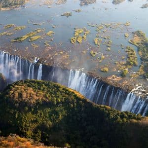 Eine Luftaufnahme eines gewaltigen Wasserfalls, der über eine breite, lange Schlucht stürzt, umgeben von einer üppigen grünen und braunen Landschaft.