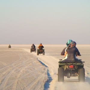 Eine WeRoad-Gruppenreise mit Quad-Bikes, die in einer Reihe über eine weite, weiße Salzpfanne unter klarem Himmel fahren.