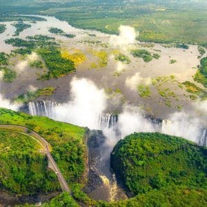 Luftaufnahme eines gewaltigen Wasserfalls an einem breiten Fluss, der in eine tiefe Schlucht stürzt und Nebelwolken über einer grünen Landschaft bildet.