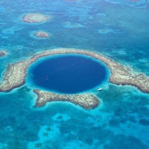 Eine Luftaufnahme einer großen, kreisförmigen Meeresdoline mit tiefblauem Wasser, umgeben von einem Korallenriff in einem türkisfarbenen Meer.