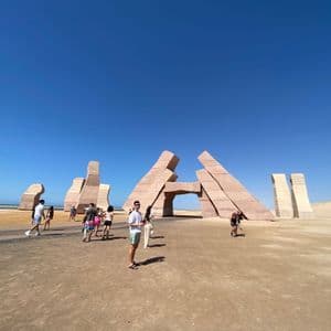 Un viaje en grupo de WeRoad explora grandes esculturas de piedra abstractas en un paisaje desértico bajo un cielo azul claro.