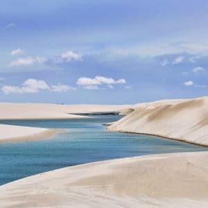Una vibrante laguna blu si snoda tra estese dune di sabbia bianca sotto un cielo punteggiato da soffici nuvole bianche.