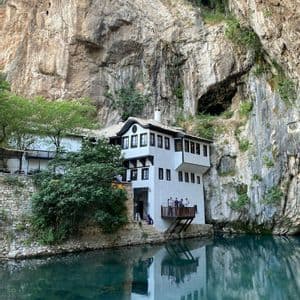 Un tradizionale edificio bianco costruito alla base di una ripida scogliera rocciosa, con il suo riflesso visibile nelle calme acque turchesi sottostanti.