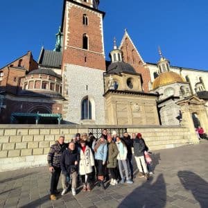 Un grupo de WeRoad posa para una foto en una plaza adoquinada frente a una gran catedral de ladrillo bajo un cielo azul claro.