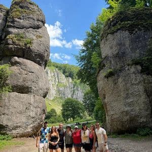 Un viaje en grupo de WeRoad posa para una foto en un sendero de tierra entre dos grandes formaciones rocosas cubiertas de musgo bajo un cielo azul.