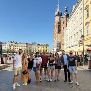 Un viaje en grupo de WeRoad de ocho personas posando para una foto en una soleada plaza adoquinada de la ciudad con edificios históricos al fondo.