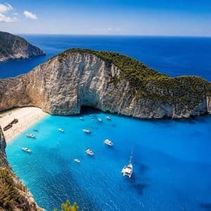 Una vista aerea di una caletta isolata con una spiaggia di sabbia bianca, un relitto e numerose imbarcazioni sull'acqua turchese.