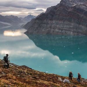 Un gruppo WeRoad di escursionisti su un fianco roccioso che si affaccia su un fiordo turchese, costellato di piccoli iceberg, sotto un cielo nuvoloso.