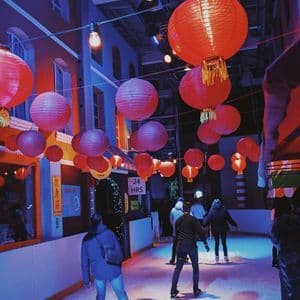 Un viaggio di gruppo WeRoad per pattinare sul ghiaccio su una pista al coperto, illuminata da luci blu e viola e decorata con lanterne di carta rosse.