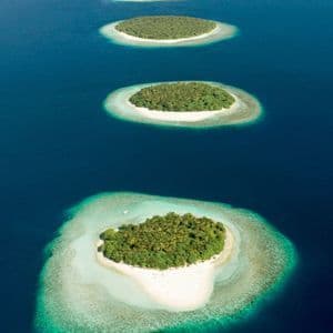 An aerial view of a line of small tropical islands with coral reefs surrounded by deep blue water.