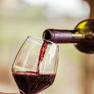 Un primo piano di vino rosso versato da una bottiglia in un bicchiere da vino su uno sfondo leggermente sfocato.
